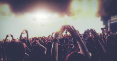 siluetas borrosas de la multitud de conciertos en la vista trasera de la multitud del festival levantando las manos en las luces brillantes del escenario foto