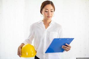 mujeres asiáticas ingenieras inspeccionando y trabajando y sosteniendo planos en la oficina. ella sonríe feliz por el trabajo foto