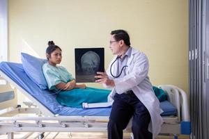 el médico está explicando los resultados de la radiografía del cerebro a una paciente acostada en la cama de un hospital foto