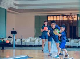 padre enseñando a su hijo y a su familia a jugar bolos en el club de bolos en tiempo de relajación foto