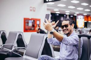 hombre asiático con viajero de mochila usando el teléfono móvil inteligente para videollamadas y tomando en un aeropuerto foto