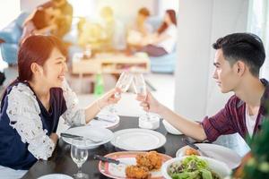 pareja joven asiática disfrutando de una cena romántica tomando una copa mientras se sienta en la mesa de comedor en la cocina juntos foto