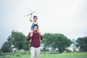Niña asiática y padre con una cometa corriendo y feliz en la pradera en verano en la naturaleza foto