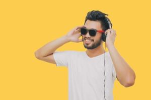 hombre guapo asiático con bigote, sonriendo y riendo y usando un teléfono inteligente para escuchar música con auriculares con fondo amarillo foto