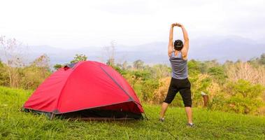 un hombre hace ejercicio y un atleta se calienta por la mañana cerca de una tienda de campaña en un viaje de campamento en la montaña foto