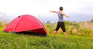 un hombre hace ejercicio y un atleta se calienta por la mañana cerca de una tienda de campaña en un viaje de campamento en la montaña foto