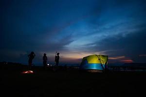 Silhouette  group of Asian friends tourist drinking and playing guitar together with happiness in Summer while having camping near lake photo