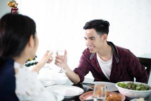 pareja joven asiática disfrutando de una cena romántica tomando una copa mientras se sienta en la mesa de comedor en la cocina juntos foto