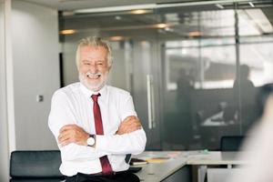 Happy handsome old businessman standing and smiling in office photo