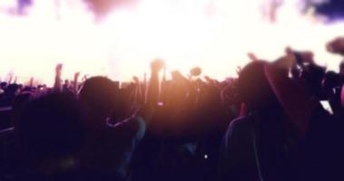 siluetas borrosas de la multitud de conciertos en la vista trasera de la multitud del festival levantando las manos en las luces brillantes del escenario foto