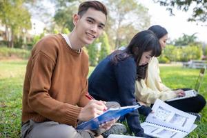 Grupo de estudiantes universitarios asiáticos sentados en la hierba verde trabajando y leyendo juntos al aire libre en un parque foto