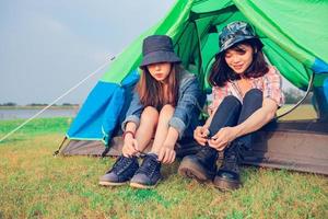 A group of Asian friends tourist Tie a shoe near tent with happiness in Summer while having camping photo