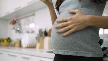 schwangere frau berührt den bauch, während sie das smartphone in der küche benutzt