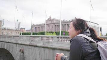 mujer asiática de pie y viendo una hermosa vista del río en suecia, de pie junto al río. viajar al extranjero de vacaciones. el puente sobre el río con fondo de construcción video