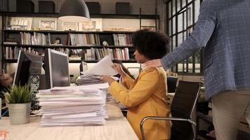 drukke vrouwelijke werknemer, jong afro-amerikaans personeel is hard aan het werk met veel stapel documenten en papierwerk op het bureau, overbelasting werkte onvermoeibaar voor de deadline van het werk in de werkruimte van het kantoor. video