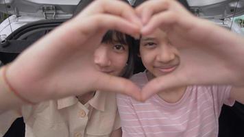 Two girls making hand gesture heart shape together and looking at camera. video