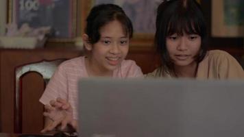 Two teen sisters playing video games online on laptop at home.