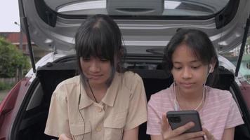 Two teen girls watching social video online on mobile smartphone with earphones.