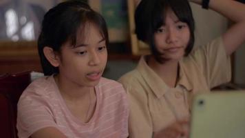 Two girls enjoy chatting to friends with video call on digital tablet at home.