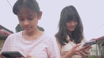 Two girl sibling enjoy using and texting on mobile smartphone. video