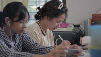 una adolescente aprendiendo una lección en línea con una tableta digital mientras su hermana menor juega juegos en línea en un teléfono inteligente. video