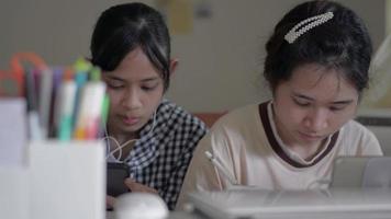 Girl helping her sister searching useful information from website on smartphone during study at home. video