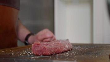 chef aplicando sal granulada en un trozo de bistec crudo. video