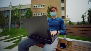 Young businessman with mask using laptop, at campus outdoors.