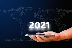 mano que sostiene el teléfono inteligente con blanco 2021 en el mapa mundial. año nuevo y concepto de tecnología. foto