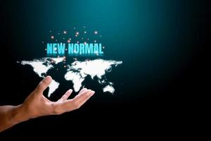Hand holding white world map with blue text 'new normal' and orange light on blue and black technology background. New normal concept. photo