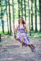 Hippie style girl swings on swing in the woods photo