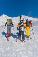 amigos con esquís y tablas de snowboard suben la colina con raquetas de nieve y pieles de foca foto