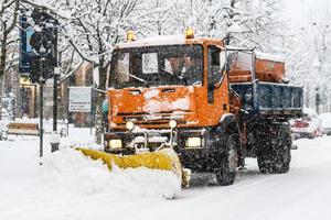 A snow plow at work during snowfall on whitewashed streets in the city photo