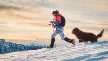 chica deportiva con su perro durante un trekking alpino en la nieve
