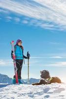 Dog in the mountains in the snow with mistress in alpine skiing photo