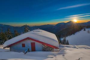 cabaña alpina en la nieve durante la puesta de sol foto