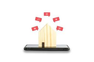 Business and technology at home concept. Small wooden home on black mobile or smartphone with red pop up icon of application isolated on white background. Clipping path photo