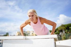 Mature woman working strength training push ups against sky with copyspace. photo