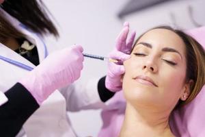 Doctor injecting hyaluronic acid into the cheekbones of a woman as a facial rejuvenation treatment. photo