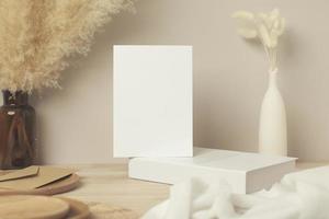 Blank paper card, greeting card mock up. decoration with dried Bunny Tail and pampas grass, Front view, Beautiful Bunny Tail grass in vase and white book on wood table and beige cement wall background