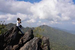 mujer sentada en las rocas usando una cámara para capturar imágenes de montañas en verano foto