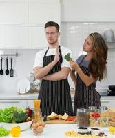 joven mujer caucásica alimentando vegetales frescos a su novio en la cocina. pareja juntos concepto foto