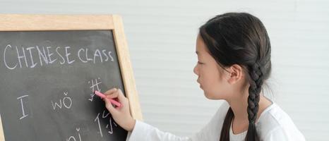 Asian Girl Writing Chinese Alphabets on Blackboard in Classroom