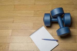 A healthy mind in a healthy body. A paper notebook and a dumbbell on a wooden floor. photo