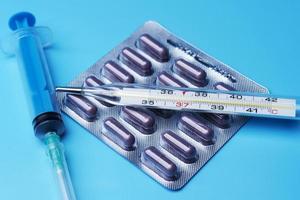 Syringe, pills and a thermometer on the blue background. photo