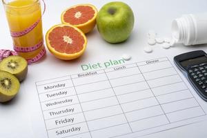 Diet plan on a piece of paper, next to a glass of orange juice. Fresh grapefruit, kiwi and Apple with centimeter on white background. photo