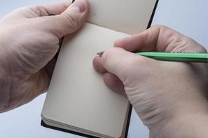 Hands of a man holding a notebook and a pen on a white background.