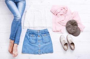 Casual summer outfit with different accessories and female legs in jeans on white wooden floor. Top view and copy space. photo