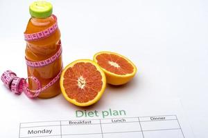 plan de dieta y botella de jugo de toronja con toronja fresca sobre fondo blanco. foto