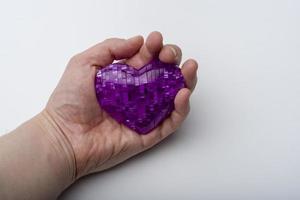 The hand holds the heart on a white plastic background. photo